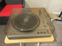 Turntable with closed smoke-tinted acrylic dust cover on wood-veneer and metal chassis