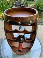Front view of barrel-shaped wooden wine bottle stand holding 8 bottles, showing slatted shelves and single bottle