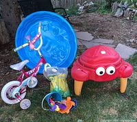 Child's outdoor play items on grass, including bike, sandbox, sandbox toys, wading pool, and bag of sand.