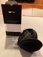 Black Zerogrand Cole Haan Bluetooth ear warmers displayed next to open original packaging box on white surface.