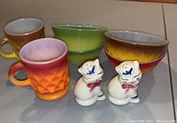 Overall lot showing Kimberly Diamond mugs and bowls in warm orange/yellow/brown gradients, green ombré bowls, and Shawnee ceramic cat salt and pepper shakers.
