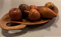 Photo showing a side angle of the wooden fruits displayed in the hand-carved wooden bowl with handle, exhibiting the sizes, colors, and textures of the fruits and bowl.