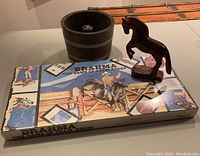 Photo showing three items: the sealed Brahma rodeo board game, the wooden horse figurine, and the wooden nut cracking bowl shaped like a barrel.