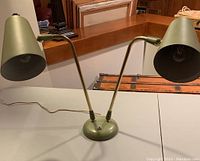 Front view of vintage MCM double gooseneck table lamp in avocado green on table, showing both arms extended with shades and base with switch.