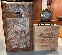Photo showing a vintage wooden wine box with world map design, a Chateau Lhorens Bordeaux wooden wine box, and a Rue Juliette clock sitting on top.