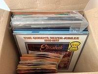 Box of vintage albums and 45s with visible album covers starting with 'The Queen's Silver Jubilee 1952-1977 Elizabeth II' on top and paper sleeves of 45 singles in front.
