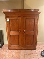 Front view of wooden armoire with two doors and white knobs, showing paneled wood design and aged finish.