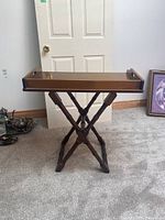 Front view of a wooden butlers table with removable tray top, positioned in front of a white door on carpet.