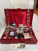 Full view of costume jewellery collection inside a red wooden box with red velvet interior, various necklaces, earrings, and brooches visible on bed and in box.