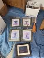 Five framed artworks and one decorative bottle on blue padded cloth with boxes in background