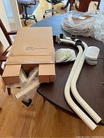 Overview of EZ Mover furniture moving kit parts on a table including two curved white metal bars, wheels, pads, and packaging boxes.