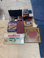 Wide view photo of all games including sealed Monopoly, Scrabble games, poker chips in black case, vintage Chinese checkers board, and various boxed games.