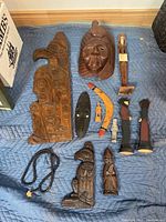 Full overview of lot showing carved wood panels, masks, boomerang, figurines, and necklace.