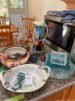 View of all items including bowls, pitcher, glass plates, trivet, and glass box on countertop