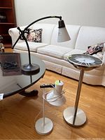Photo showing two desk lamps on a glass table next to a standing clock sidetable with round clock face top.