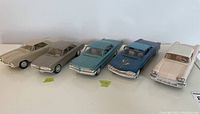 Five plastic model cars on a white surface, showing various colors and styles from late 1950s and early 1960s Pontiacs and Buicks.