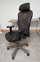 Side view of high-backed office chair showing black leather seat and headrest, mesh back, adjustable armrest and base with casters.