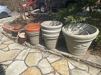 Several groupings of planters including a very large gray resin planter with leaf motifs, medium gray planters stacked inside, and smaller terracotta and plastic planters in the background.