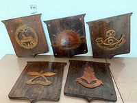 Five wooden British regimental plaques displayed together showing detailed brass insignia and badges from WWI and WWII.