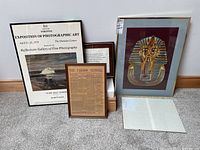 Four framed art pieces and one clip frame grouped together against a white wall showcasing the lot contents.