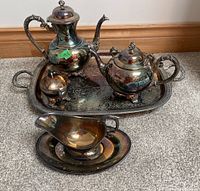 Silver plate coffee and tea serve ware set arranged on large serving tray and carpet floor, showing tarnishing and wear