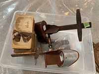 Photo showing two stereoscopic viewers, one wooden with broken/missing handle, another metal with an engraved body and wooden handle, plus a bundle of old stereoscopic cards tied with a ribbon.