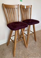 Two wooden swivel bar stools side by side showing slatted backs and burgundy faux suede seats