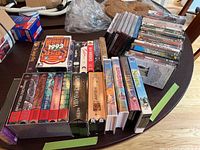 Photo showing assorted VHS tapes and DVDs laid out on a table. VHS include box sets like The 10 Commandments and Lawrence of Arabia. DVDs include Shrek and Anastasia.