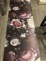 Full view of one wallpaper panel showing large pink, white, and maroon flowers and green leaves on dark background, lying on wooden floor.