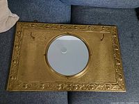 Full view of the vintage hammered brass mirror hat rack showing rectangular frame, central round mirror, and two hooks.