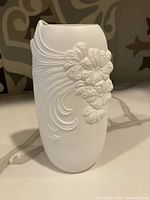 Front angle showing embossed floral and swirl textural design on white ceramic vase.