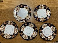 Overview of all five vintage Royal Albert Crown China plates showing decorative cobalt blue border with floral and gold accents
