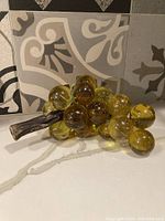 Full view of the vintage mid century acrylic grape cluster showing the amber grape spheres attached to the faux stem and green leaves.