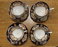 Overhead view of four tea cups and saucers arranged on a wooden table, showing floral and gold designs with navy blue backgrounds.