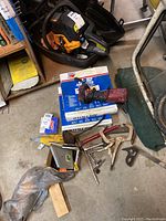 Photo showing various tools including a drill, clamps, air filter boxes, and other hand tools arranged on a surface.