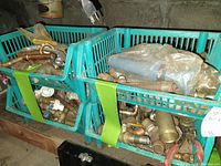 Overview of two teal plastic baskets containing various brass plumbing fixtures and parts including valves, fittings, and pipe sections.