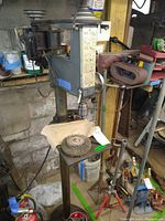 Front view of Craftsman drill press mounted on metal stand, showing sanding belts and wire brush wheel on table.
