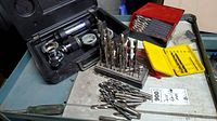 Overview photo showing several drill bit sets in metal and plastic holders alongside a cooling system tester in a black case.