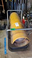 Yellow gas powered heater in metal frame, showing front and side with handle grip and base.