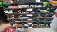 Five stacked metal drawers from a tool chest labeled for bolts, plumbing, and hardware items, showing general weathered condition