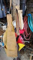 Leather aprons, tool bags, plastic funnels, and coiled garden hoses hanging on hooks in a workshop setting.