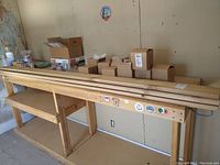 Three pieces of plywood lumber placed on a wooden workbench with some boxes in the background.