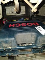 Closed Bosch planer case with visible dust and wear, red Bosch label on blue plastic case.