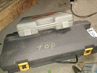Gray plastic Ryobi reciprocating saw case marked 'TOP' with yellow latches and smaller gray carrying case on top