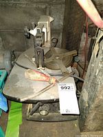 Side view of the metal bandsaw showing table surface, blade support arm, red-handled screwdriver, and blade reel.
