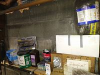 Shelf displaying multiple cans, gauges, and boxes with hardware items including labeled boxes for screws, wire brushes, and filters, along with fluids and a triple gauge pack.