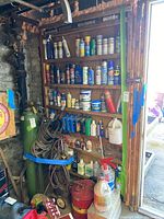 Overview of wooden shelves holding various spray cans, bottles of automotive fluids, hoses and miscellaneous containers in a basement setting.