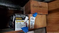 Two sealed boxes with blue tape. One labeled Respirators, two labeled Central Pneumatic High Volume Low Pressure Spray Gun 20 oz. 6 CFM.