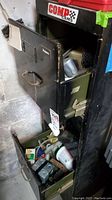 Open black metal cabinet showing some drawers filled with assorted automotive and hardware supplies.