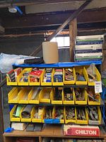 Wide view of yellow bins filled with assorted mechanical and automotive parts including spark plugs, sanding discs, valves, and fasteners